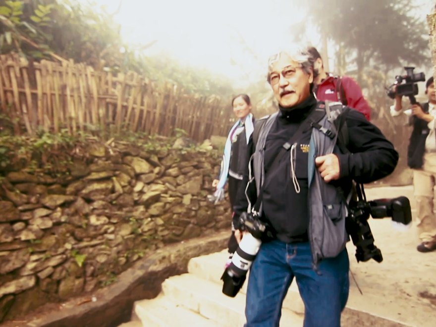 Michael Yamashita walking a village path carrying two cameras